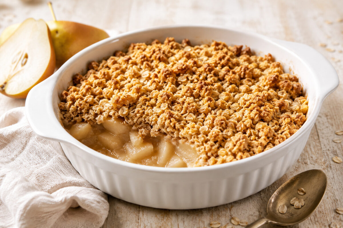 Fertiger Birnen-Crumble in weißer Keramikform mit goldbraunen Haferstreuseln und sichtbarer Birnenfüllung; Hauptansicht.
