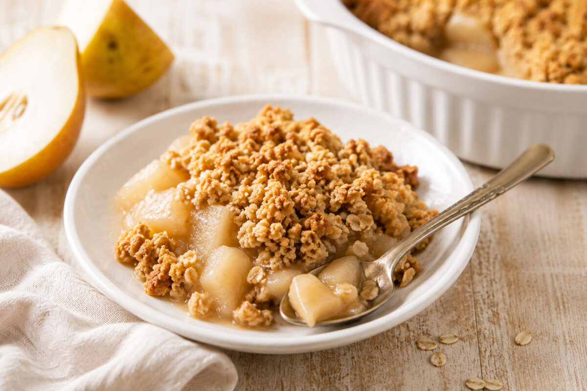 Portion Birnen-Crumble in einer kleinen weißen Schale mit Löffel; Hauptform im Hintergrund als Servierszene.