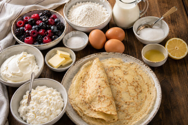 Zutaten- oder Vorbereitungsansicht mit Crêpes, Quark, Frischkäse, gemischten Beeren, Mehl, Eiern, Milch, Zucker, Zitronensaft und Butter.