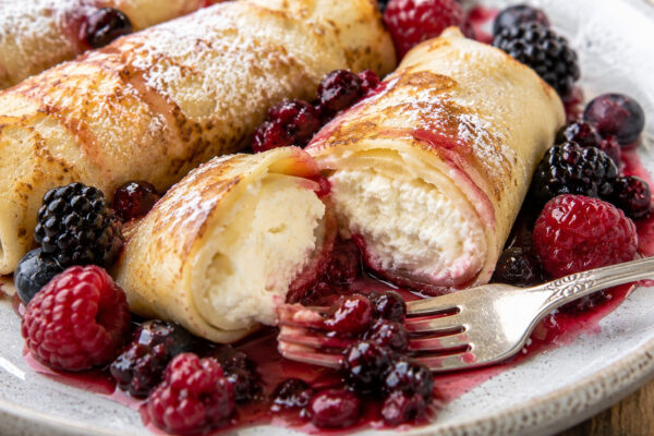 Nahe Detail- und Servieraufnahme von Blintzes mit Quarkfüllung und Beeren, mit sichtbarer cremiger Füllung und Beerenkompott.