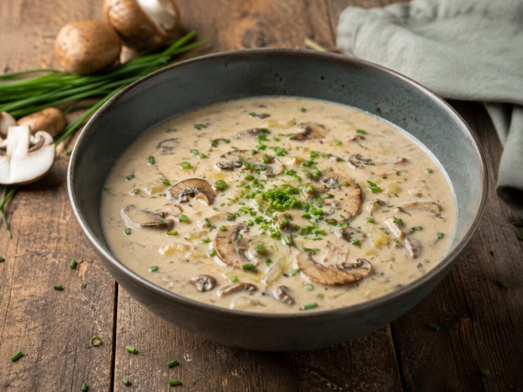 Eine cremige helle Pilz-Lauch-Suppe mit sichtbaren Champignonscheiben und grünem Schnittlauch auf der Oberfläche.