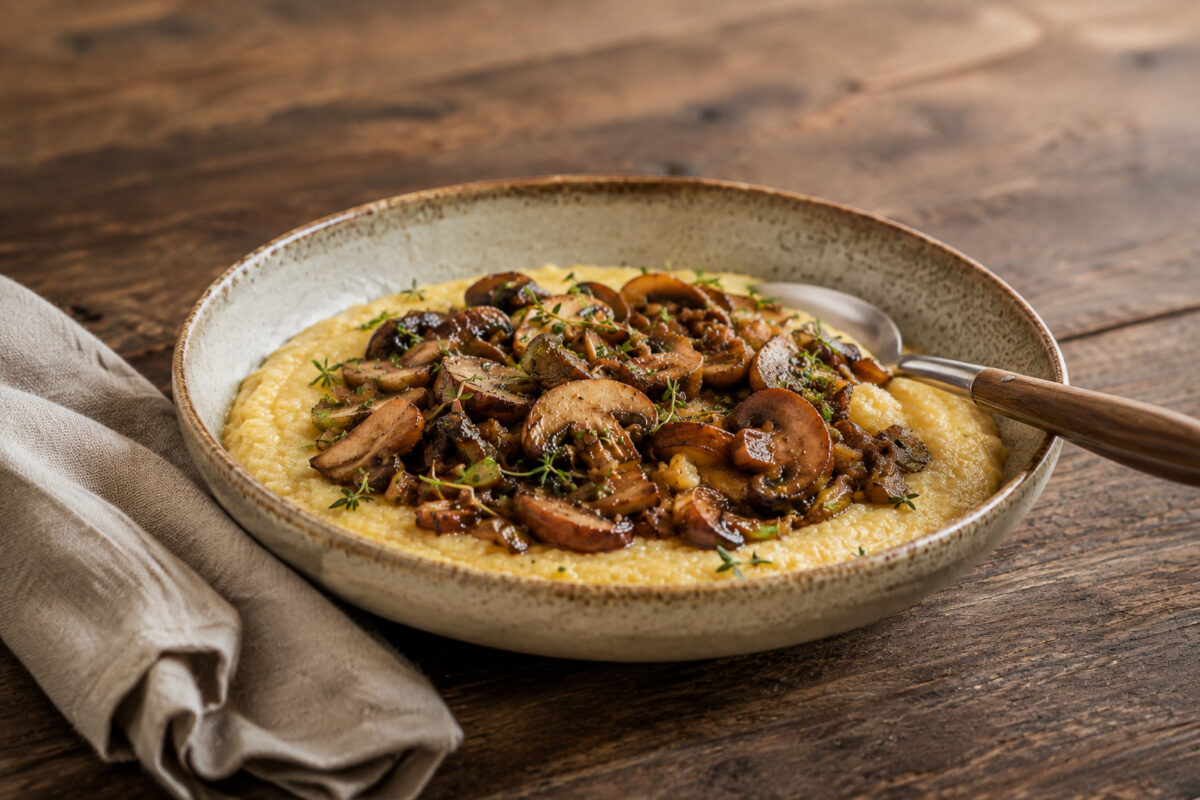 Cremige Polenta mit gebratenen Pilzen – alternative Perspektive mit Servierlöffel.