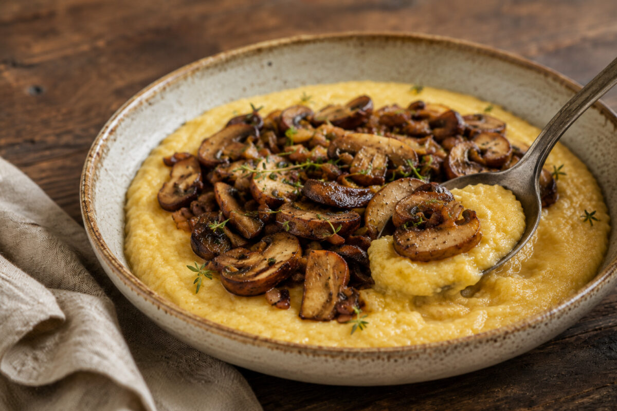 Cremige Polenta mit gebratenen Pilzen – Servierdetail mit angehobenem Löffelbissen.