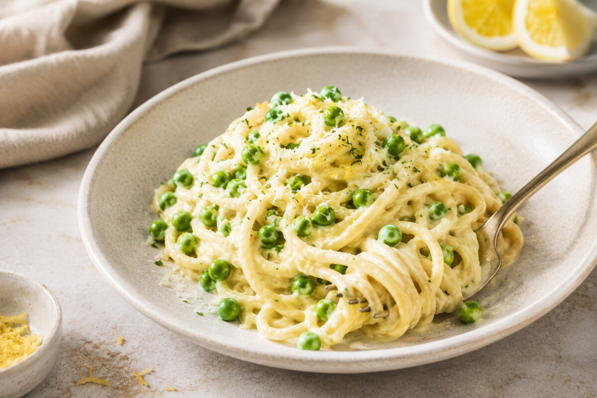 Fertige Zitronen-Pasta mit Erbsen als nahe Servier- und Detailansicht mit Gabel und Zitronenakzent im Hintergrund.