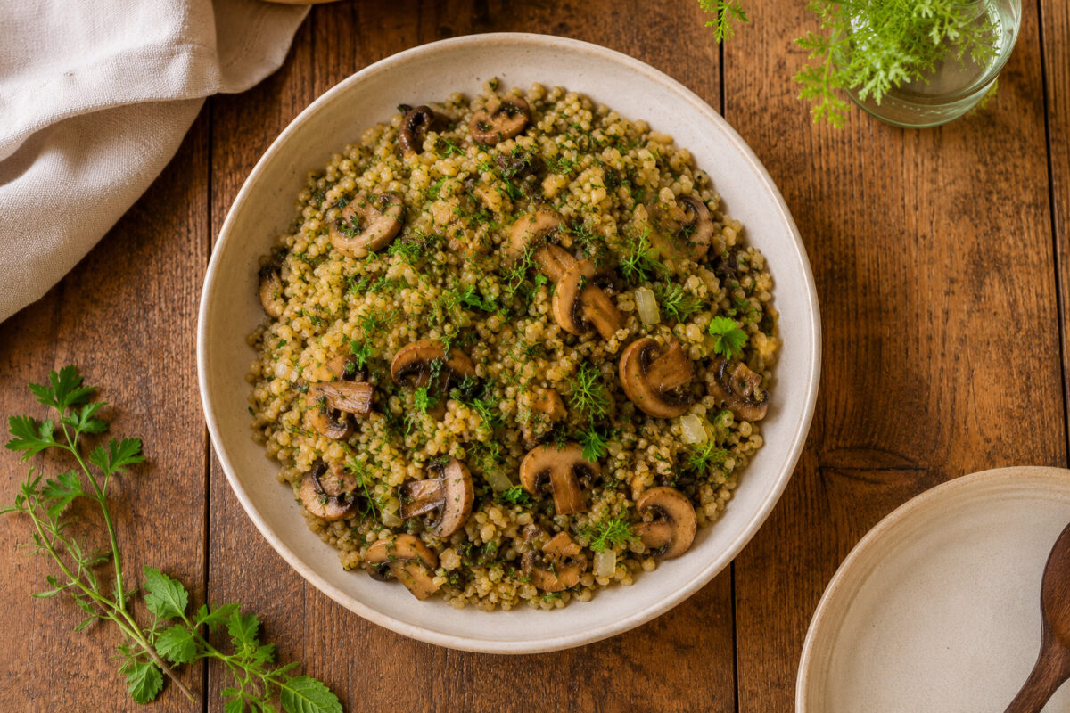 Fertiger Freekeh-Pilaw mit Pilzen und Kräutern aus deutlicher Draufsicht in derselben warm-rustikalen Bildserie.