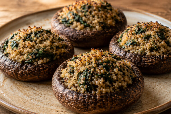 Vier fertig gebackene Portobello-Pilze mit Quinoa-Spinat-Füllung auf heller Platte.