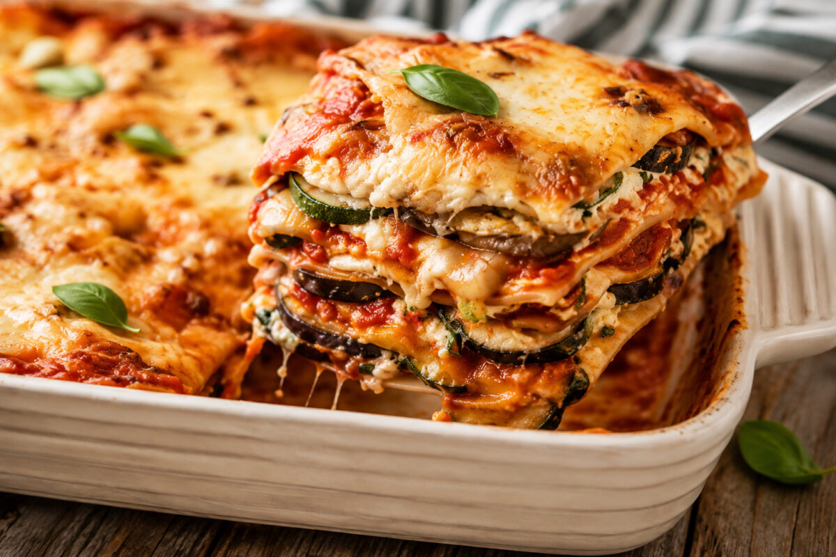 Nahes Servierdetail einer aus der Auflaufform gehobenen Portion Gemüse-Lasagne mit deutlich sichtbaren Gemüse-, Pasta-, Tomaten- und Käseschichten.