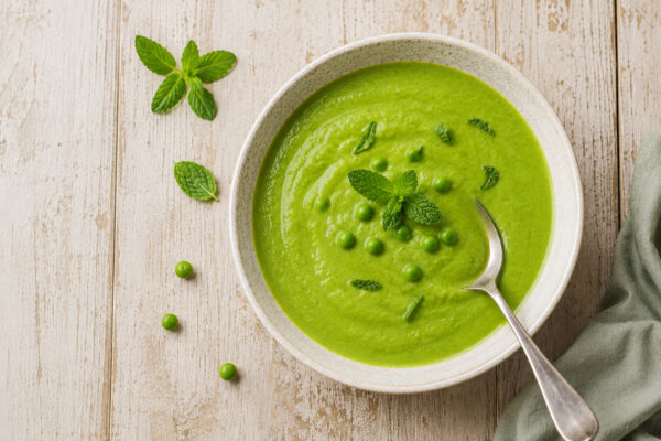 Fertige Erbsensuppe mit Minze aus deutlich stärkerer Aufsicht, mit Löffel und gleicher Keramik-, Licht- und Farbwelt.