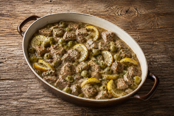 Draufsicht auf das fertige Kalbsragout in demselben ovalen Bräter mit heller Sauce, grünen Oliven, Zitronenscheiben und Petersilie.