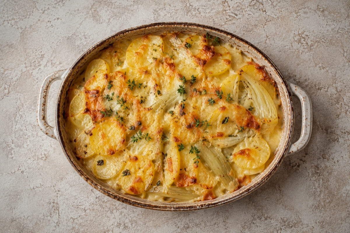 Draufsicht auf das fertig gebackene Kartoffel-Fenchel-Gratin mit goldbrauner Käsekruste in der ovalen hellen Auflaufform.
