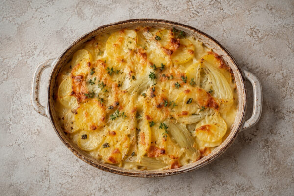 Draufsicht auf das fertig gebackene Kartoffel-Fenchel-Gratin mit goldbrauner Käsekruste in der ovalen hellen Auflaufform.
