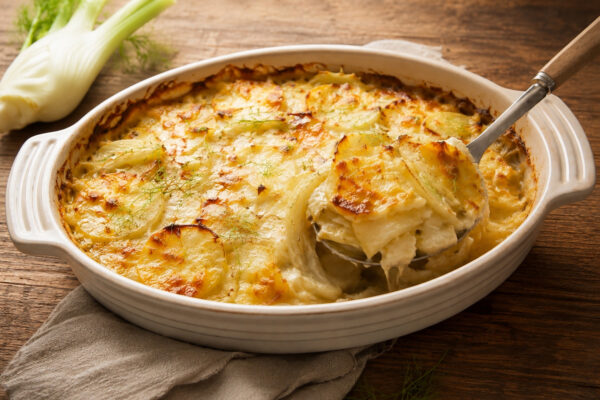 Serviersituation mit einer entnommenen Portion des Kartoffel-Fenchel-Gradins in derselben rustikalen Bildwelt.