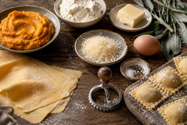 Zutaten- und Vorbereitungsansicht mit Pastateig, Kürbispüree, Ricotta, Parmesan, Ei, Butter und Salbei.