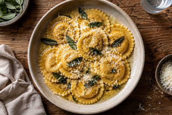 Draufsicht auf fertige Kürbis-Ricotta-Ravioli in Salbeibutter mit Parmesan.