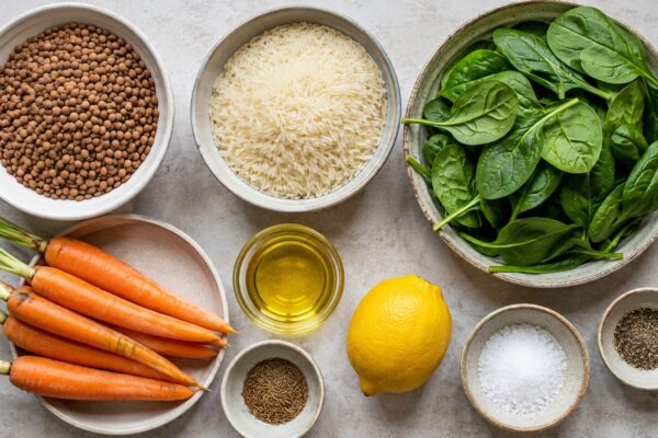 Übersicht aller Zutaten für „Linsen-Reis-Bowl mit Spinat und Möhren“ auf heller Arbeitsfläche, sauber gruppiert, ohne Verpackungsschrift und ohne fertiges Gericht.