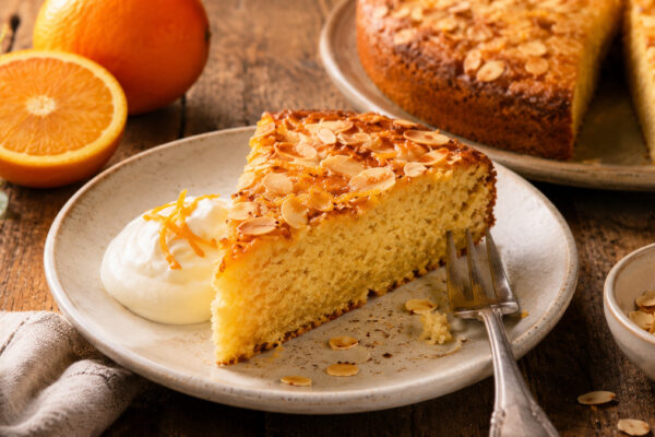 Servieransicht eines Stücks Mandel-Orangen-Kuchen mit Joghurt im gleichen rustikalen Set.