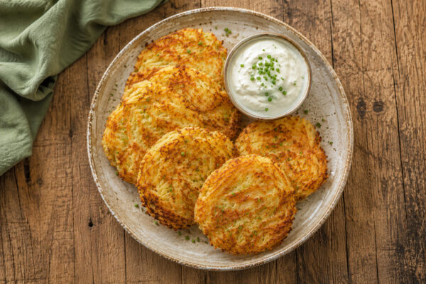 Fertige Kartoffel-Käse-Puffer mit Schnittlauchdip aus deutlich anderer, nahezu senkrechter Perspektive.