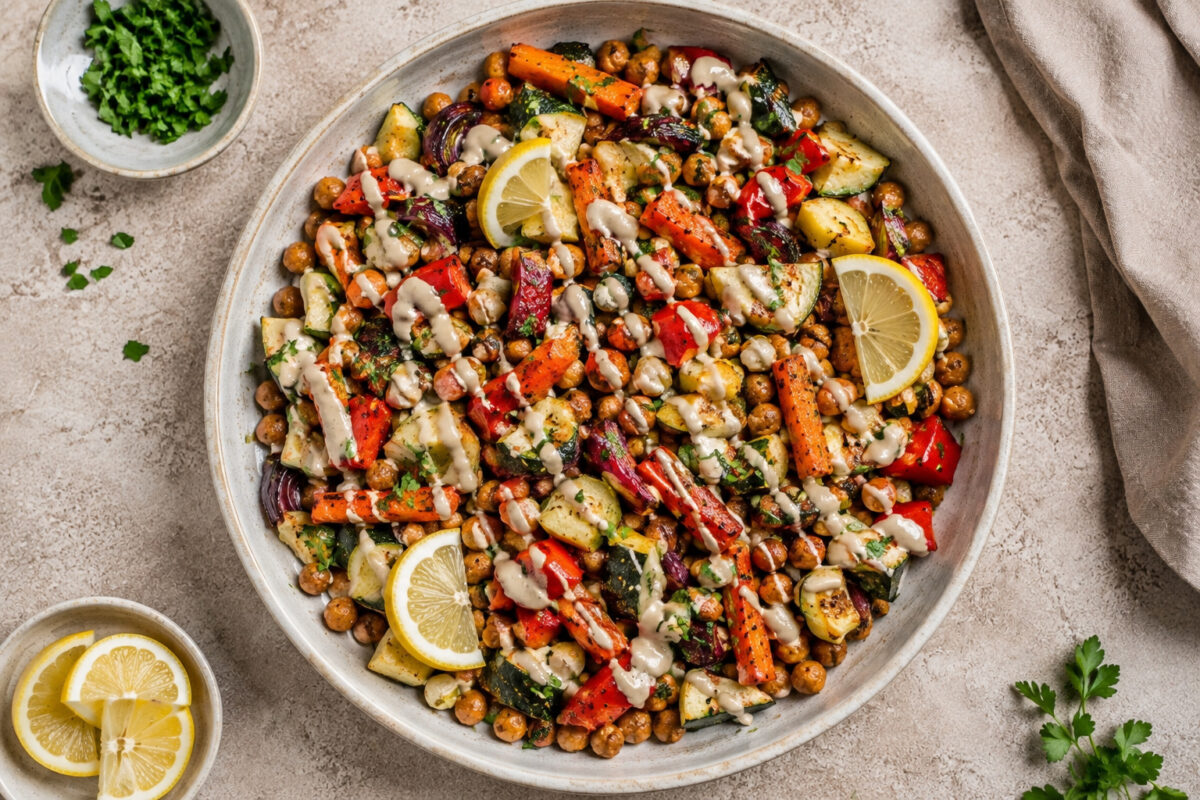 Draufsicht auf das fertige Ofengemüse mit Kichererbsen und Zitronen-Tahini in der großen flachen Keramikschale.