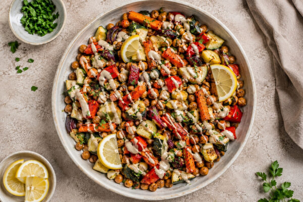 Draufsicht auf das fertige Ofengemüse mit Kichererbsen und Zitronen-Tahini in der großen flachen Keramikschale.