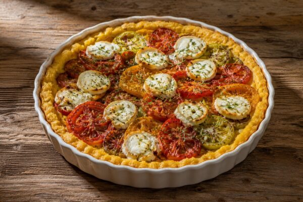 Runde Tarteform mit goldgelbem Polentaboden, bunten Tomaten und gebackenen Ziegenkäsescheiben.