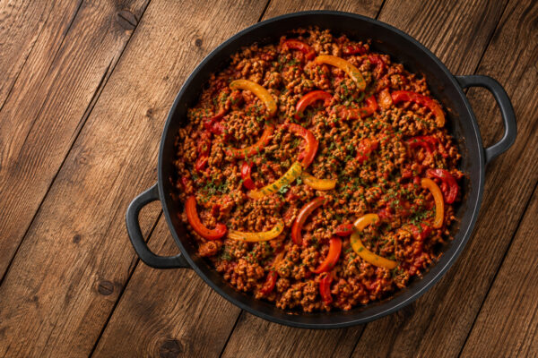 Fertige Putenhack-Paprika-Pfanne aus deutlich höherer Perspektive in schwarzer Pfanne auf rustikalem Holz.