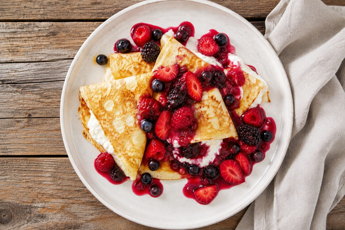 Draufsicht auf die fertigen Quark-Crêpes mit warmer Beerenkompott-Sauce auf einem großen hellen Teller.