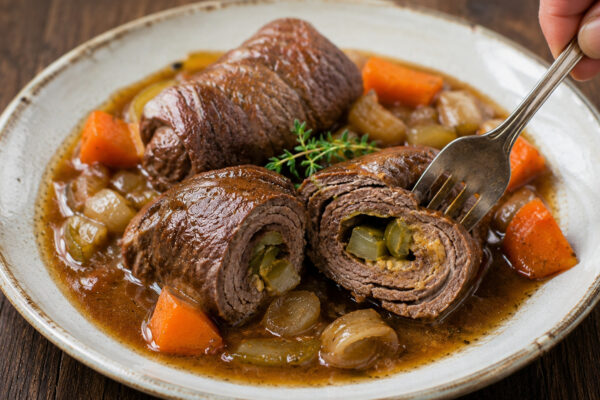 Nahe Servieransicht der fertigen Rinderrouladen mit sichtbarer Gurkenfüllung und kräftiger Bratensauce.