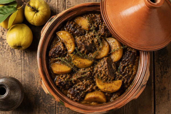 Draufsicht auf die fertige Rindfleisch-Tajine mit zart geschmortem Rindfleisch, goldenen Quittenspalten und Kräutern im Terrakotta-Gefäß.