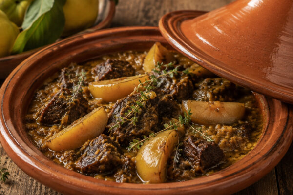 Nahe Servieransicht der fertigen Rindfleisch-Tajine mit Quitten und Kräutern im geöffneten Terrakotta-Gefäß.