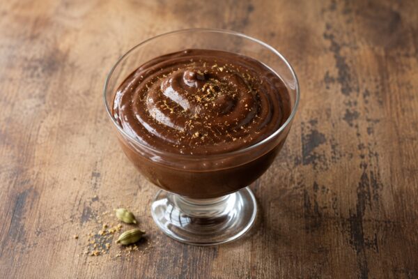 Cremiger dunkler Schokoladenpudding in einem Glasgefäß, fein mit Kardamom bestäubt.