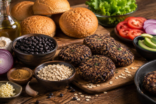 Zutaten- und Vorbereitungsansicht mit schwarzen Bohnen, Haferflocken, Zwiebel, Knoblauch, Avocado, Burgerbrötchen, Tomate und Salat.