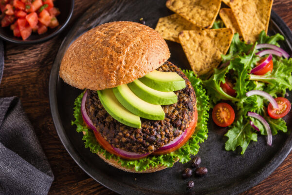 Draufsicht auf den fertigen Schwarze-Bohnen-Burger mit Avocado, Tomate, roter Zwiebel und Salat.