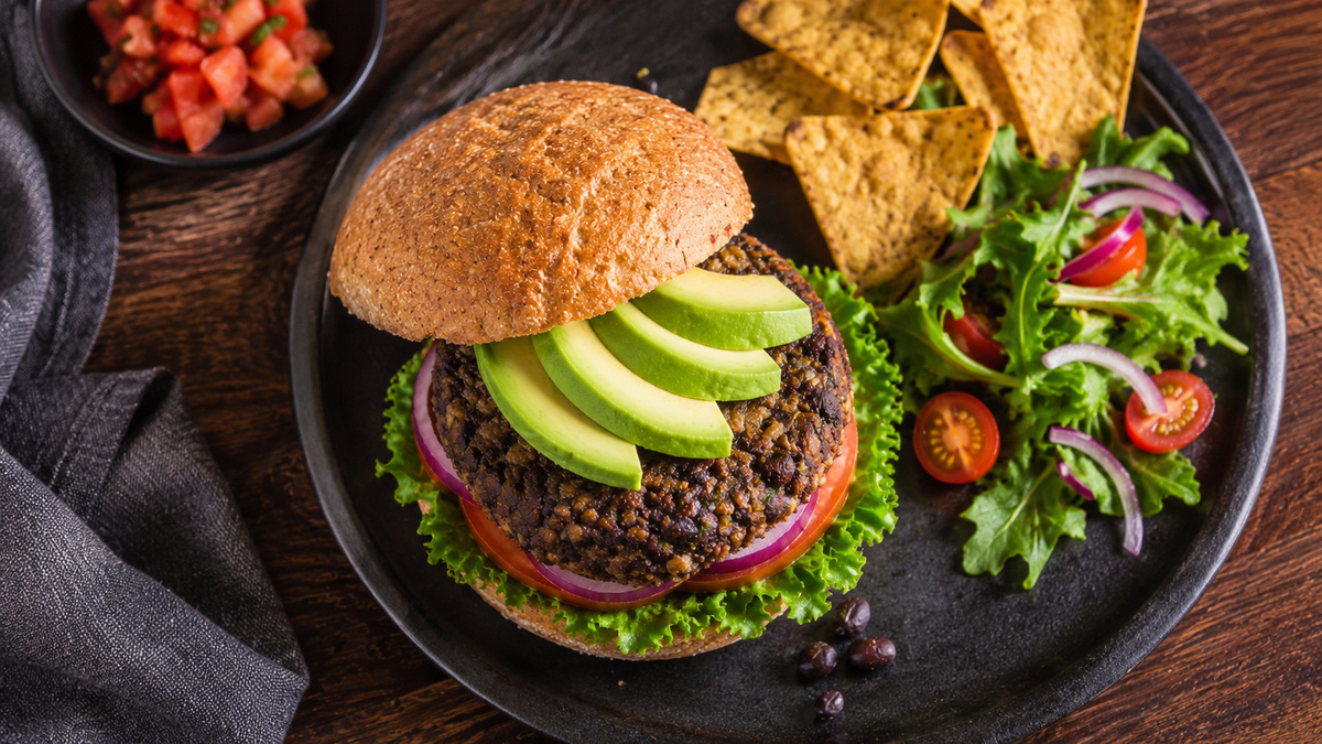 Draufsicht auf den fertigen Schwarze-Bohnen-Burger mit Avocado, Tomate, roter Zwiebel und Salat.