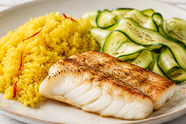 Alternative Perspektive des fertigen Gerichts: Seelachsfilet, Reis und Zucchini als komponierter Teller; die Komponenten dürfen sich leicht berühren, müssen aber einzeln deutlich erkennbar bleiben. Keine Bowl und keine homogene One-Pot-Mischung. Etwas nä…