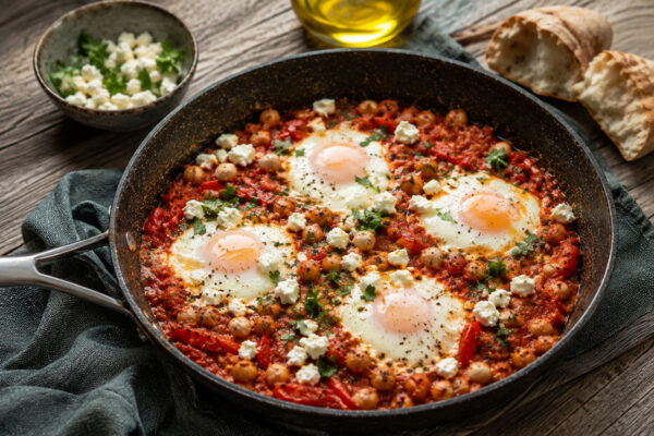 Servierszene der fertigen Shakshuka: eine Portion wird aus derselben Pfanne serviert; Tomatensauce, Kichererbsen, Ei und Feta bleiben klar erkennbar.