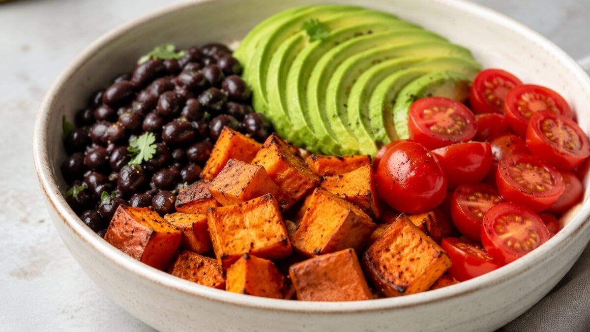 Alternative Perspektive des fertigen Gerichts: Echte Bowl mit klar getrennten Segmenten aus schwarze Bohnen, Süßkartoffeln und Avocado und Tomaten; Zutaten erst beim Essen mischbar und optisch deutlich voneinander abgegrenzt. Etwas näher aufgenommen, nat…