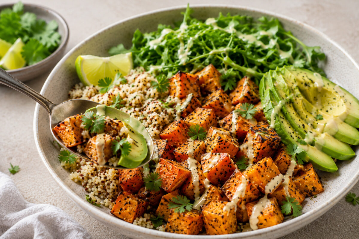 Fertige Süßkartoffel-Quinoa-Bowl als Servier-/Detailaufnahme mit Löffel und gut erkennbaren Süßkartoffeln, Quinoa, Avocado, Grün und Dressing.