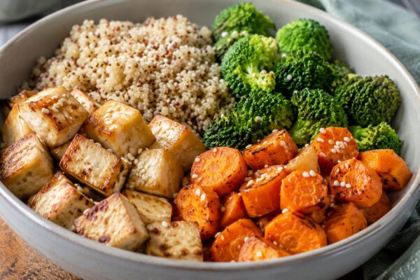 Alternative Perspektive des fertigen Gerichts: Echte Bowl mit klar getrennten Segmenten aus Naturtofu, Quinoa und Brokkoli und Möhren; Zutaten erst beim Essen mischbar und optisch deutlich voneinander abgegrenzt. Etwas näher aufgenommen, natürliche redak…