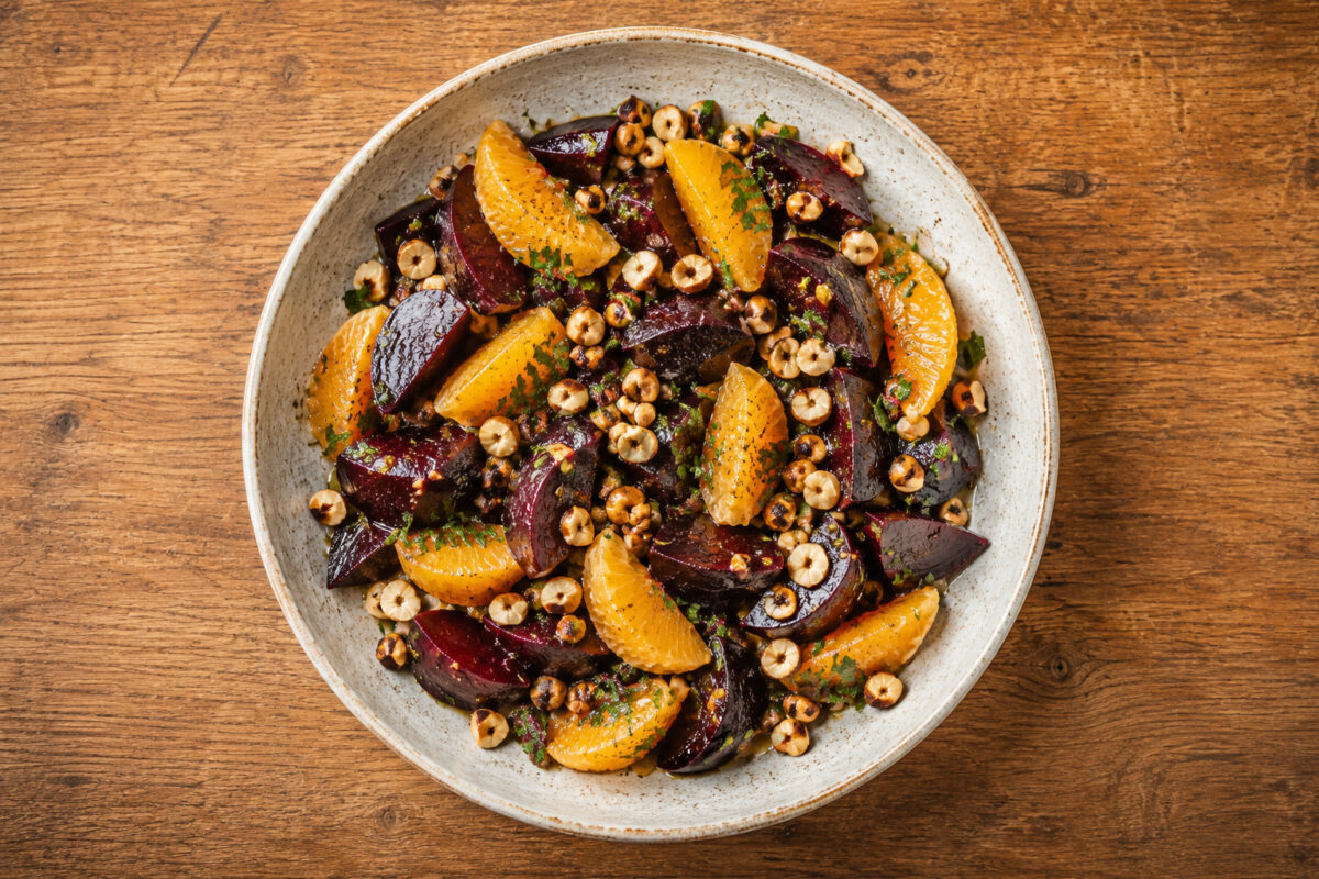 Fertiges Gericht in deutlicher Draufsicht: Rote Bete, Orangenfilets, Haselnüsse, Petersilie und Dressing vollständig in der hellen rustikalen Schale sichtbar.