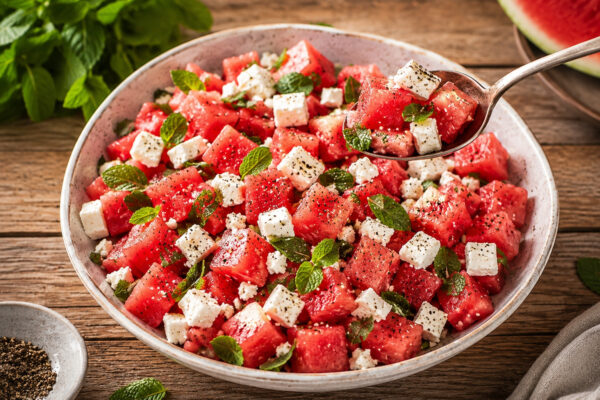 Servierszene des fertigen Wassermelonen-Feta-Salats mit Minze, mit einem Löffel entnommen.