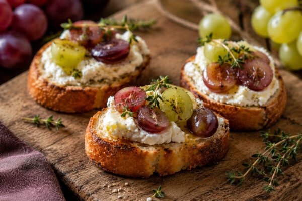 Nahe Servieransicht der fertigen Ziegenkäse-Crostini mit Trauben und Thymian.